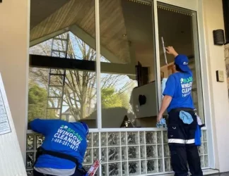 clean windows with a squeegee Two window cleaners in blue shirts and caps cleaning a large residential glass window; one using a squeegee, glass blocks at base.